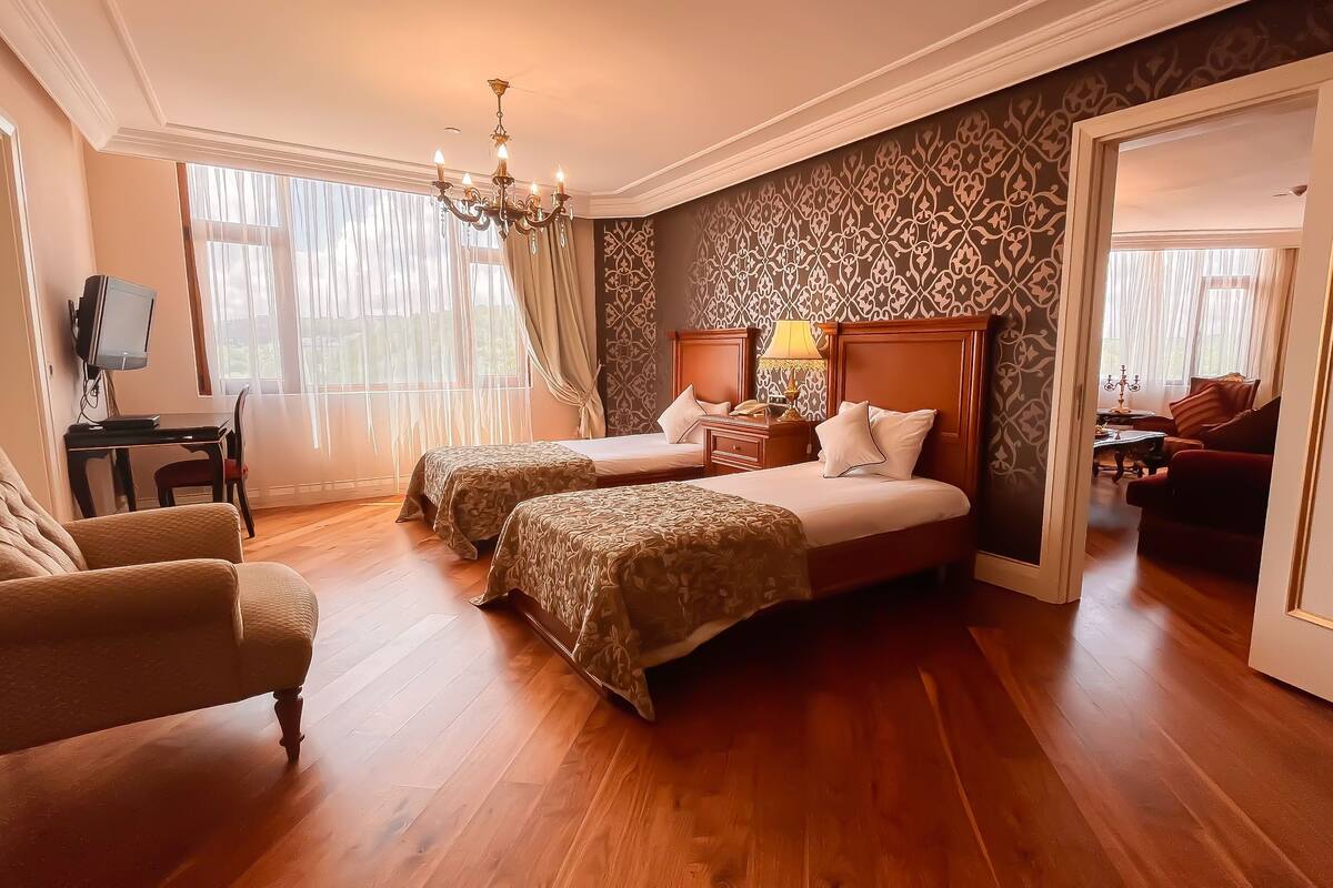 A hotel room with two beds, a desk, a chair, and a TV.