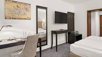 Habitación de hotel con una cama, un escritorio con una silla, una lámpara de escritorio, un teléfono, un televisor y un espejo.