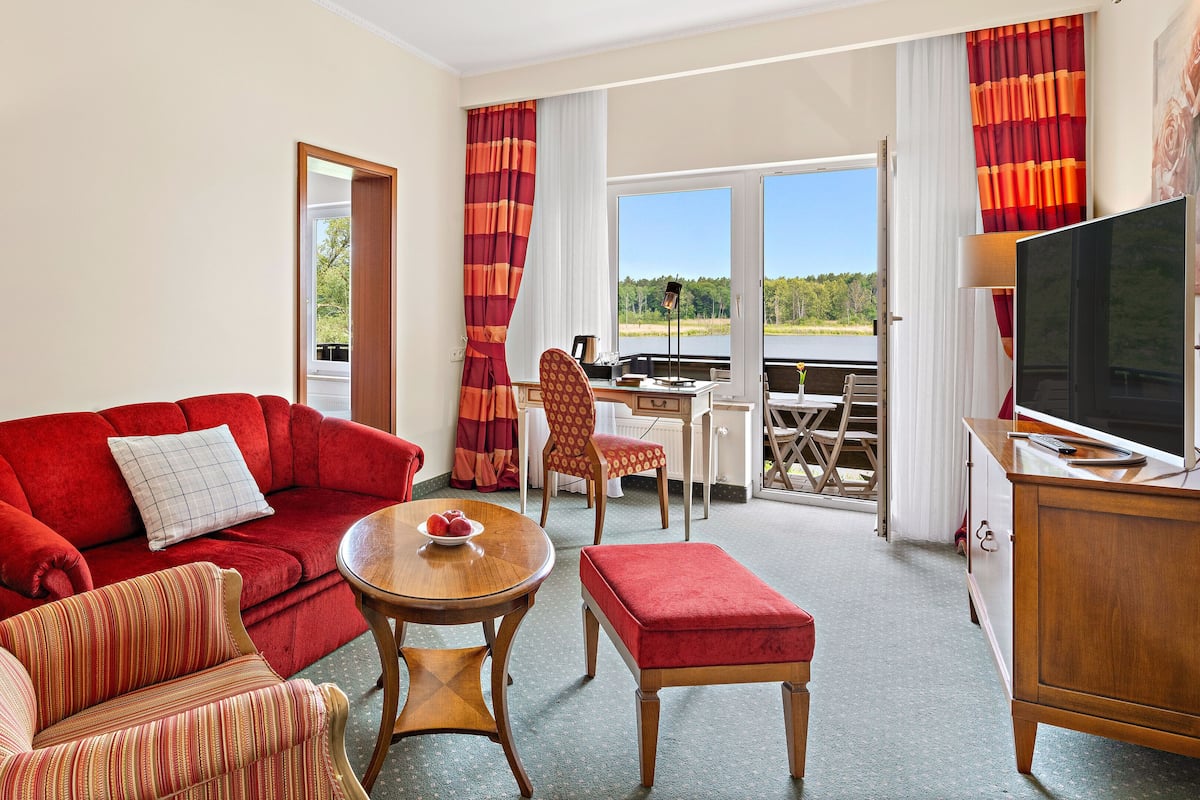 Quarto de hotel com sofá vermelho, mesa de madeira, televisão e varanda com vista para o exterior.