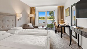 A hotel room with two beds, a desk, a chair, and a view of a lake. - Seehotel Mühlenhaus (Chorin)