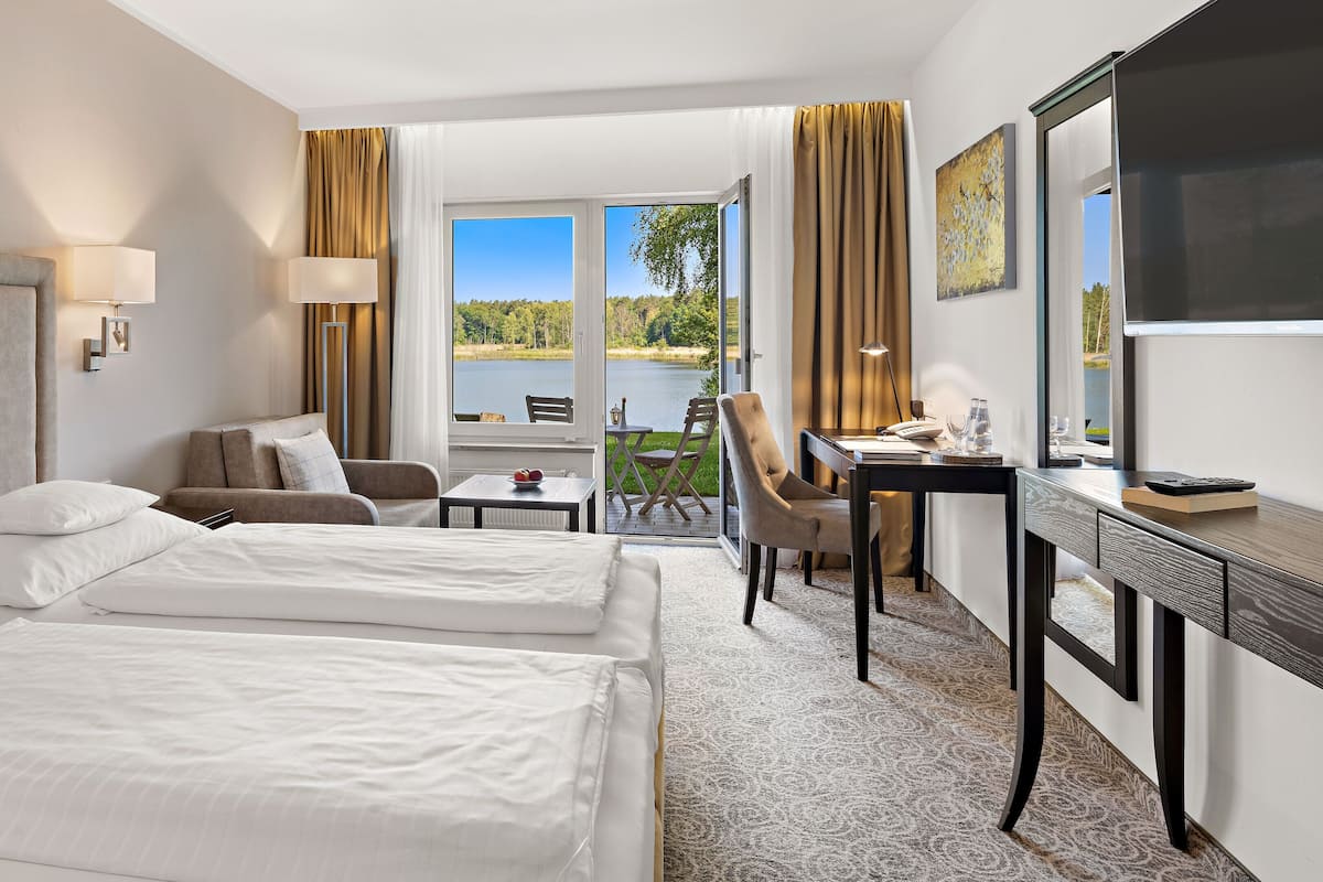 Quarto de hotel com duas camas, uma escrivaninha, uma cadeira e vista para um lago.