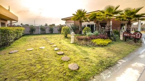 A residential area with a well-maintained lawn, stone stepping stones, palm trees, and a house with a visible address sign. - Martina Hotel (Surin)