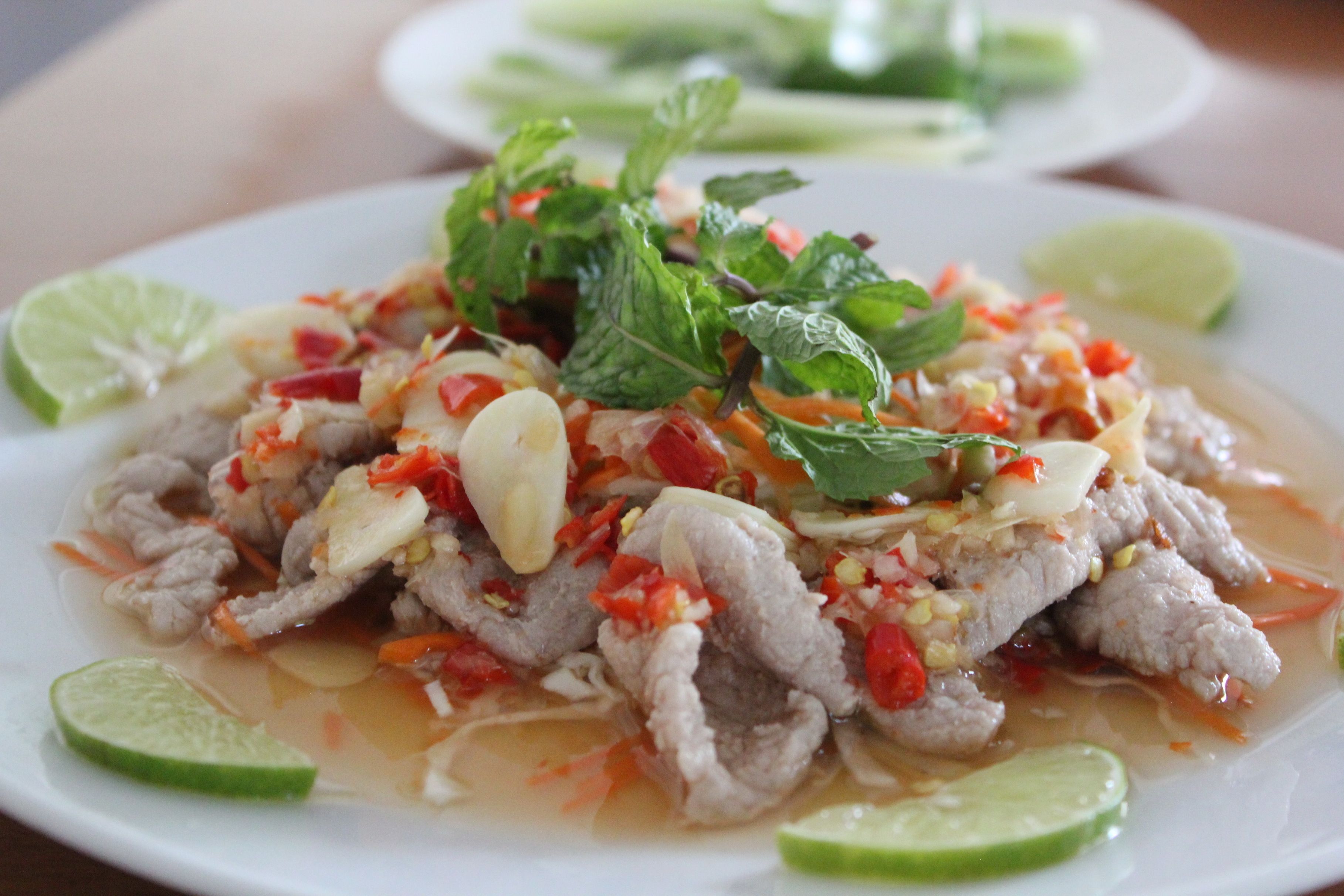 A plate of sliced meat with vegetables and herbs, garnished with lime slices.