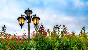 Una farola con tres luces, rodeada de follaje verde y hojas rojas.