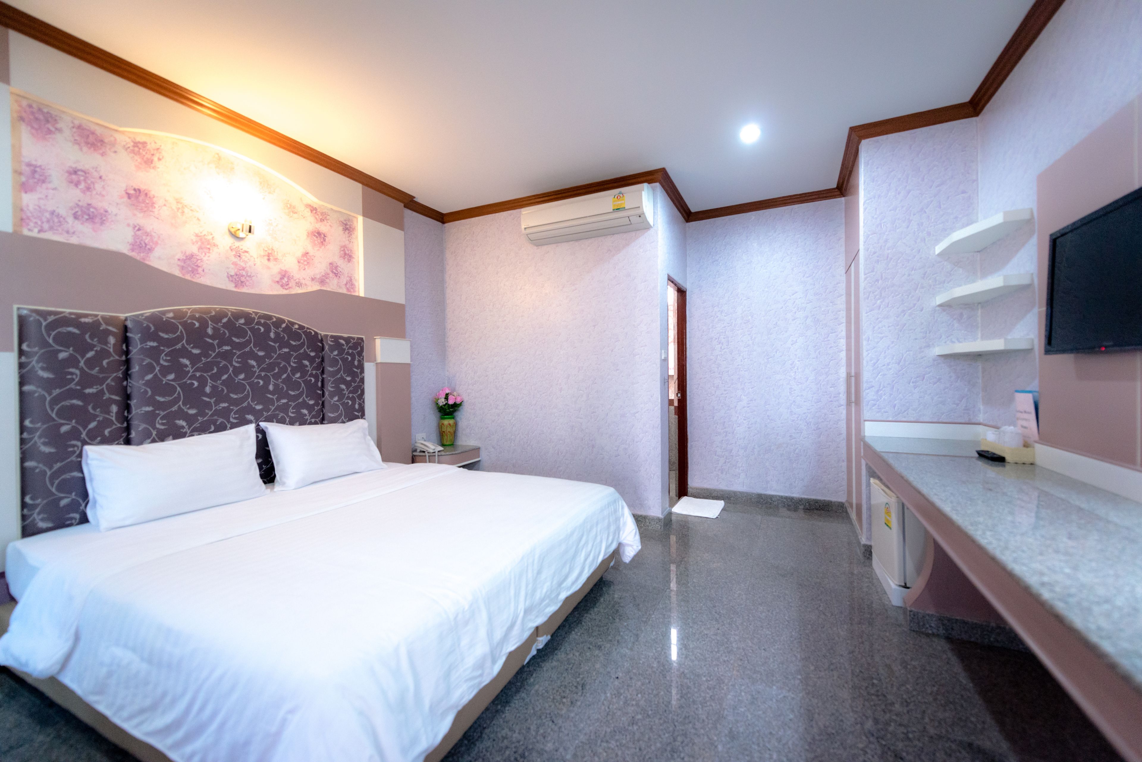 Habitación de hotel con cama, tocador con espejo, televisión y aire acondicionado.