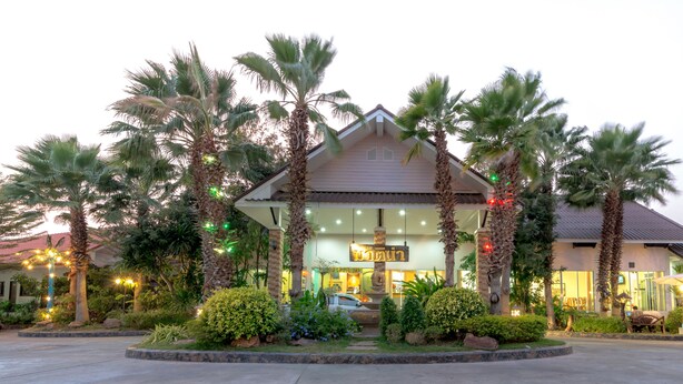 A hotel with a central entrance, surrounded by palm trees and well-lit outdoor seating areas. - Martina Hotel (Surin)
