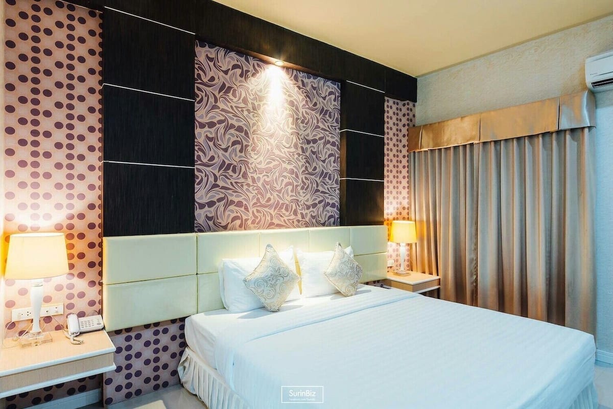 A hotel room with a large bed, two bedside tables with lamps, a patterned wall, and a curtain on the window.