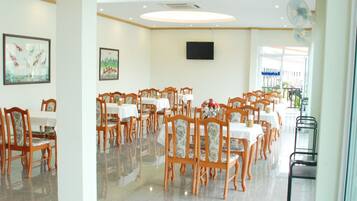 A spacious dining area with multiple tables and chairs, a polished floor, and a large fan on the wall.