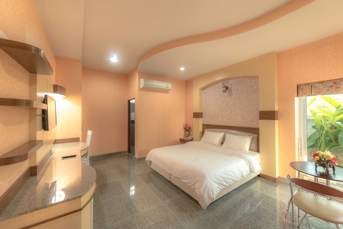 A hotel room with a bed, a desk, a chair, a nightstand, and a window with a view of greenery.