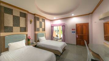 A hotel room with two beds, a small table with a chair, a wall-mounted lamp, and a door with a sign.