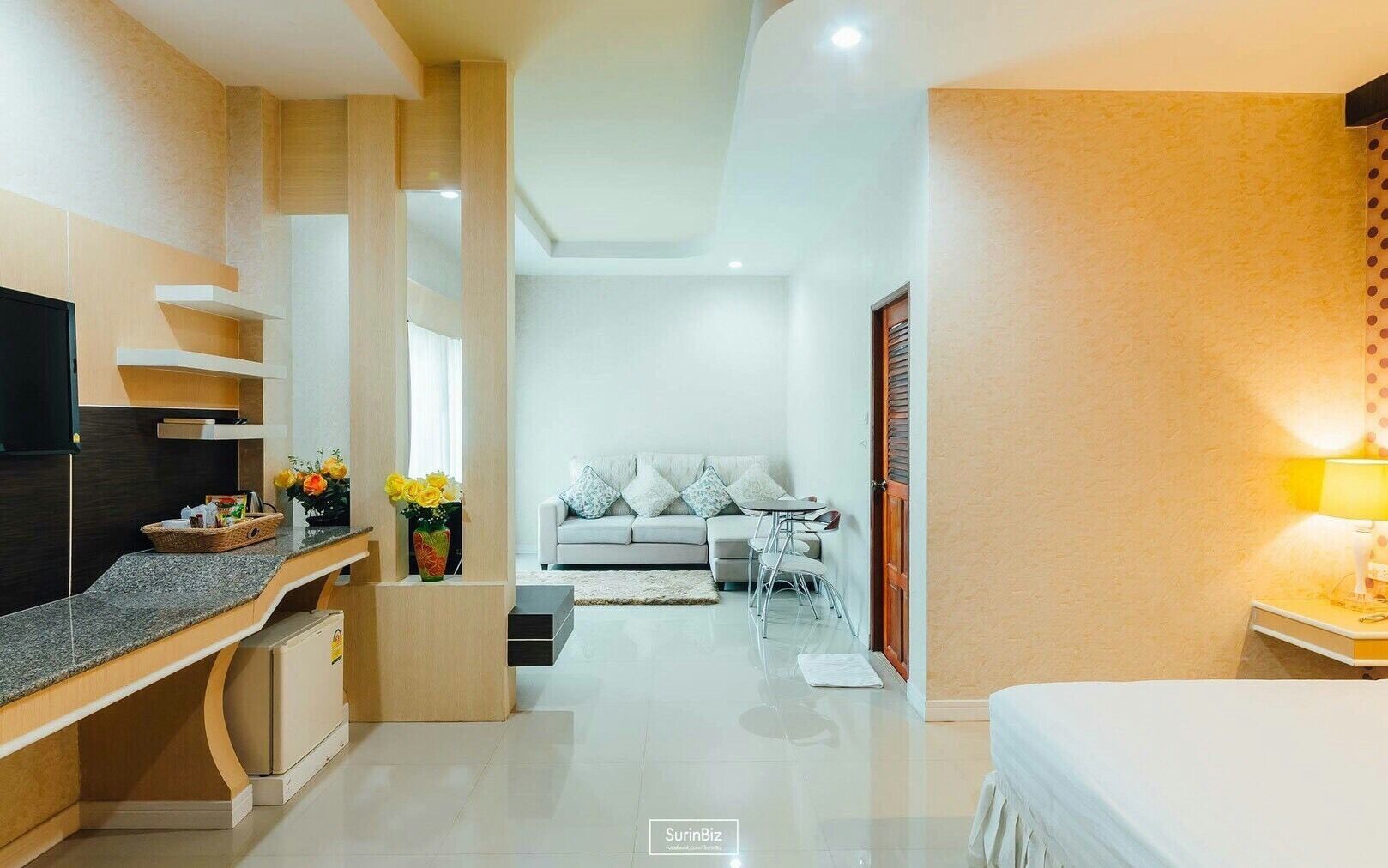 A modern hotel room with a kitchen area, a dining table, a sofa, and a TV.