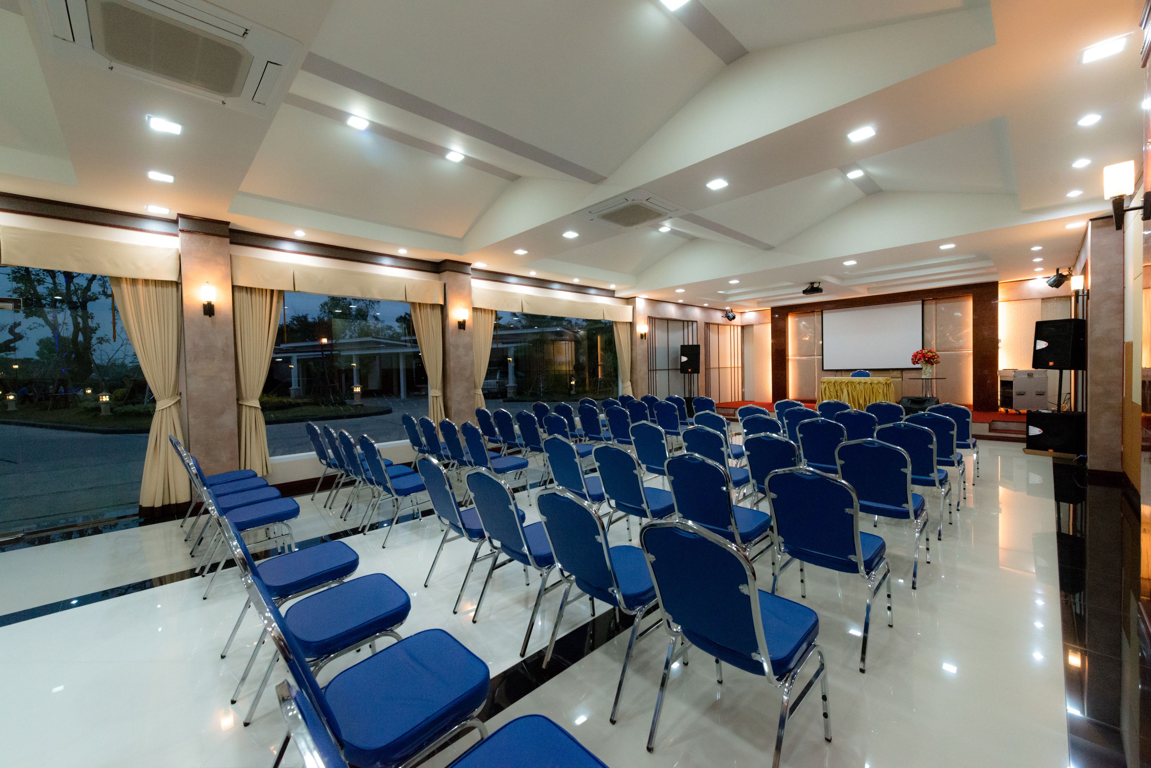 Sala de conferências com fileiras de cadeiras azuis, uma tela de projetor e palco com um púlpito.