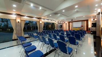 Sala de conferências com fileiras de cadeiras azuis, uma tela de projetor e palco com um púlpito.