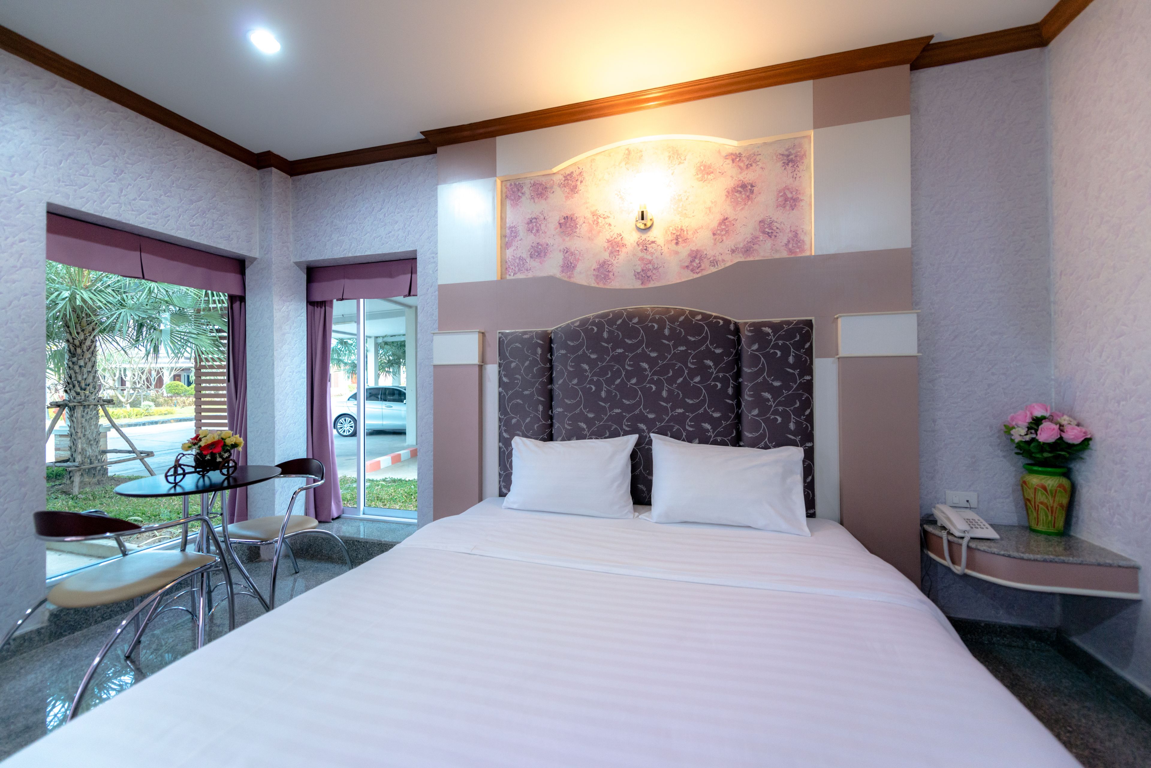 A hotel room with a large bed, a small table with chairs, a desk with a phone, and a window with a view of the outside.