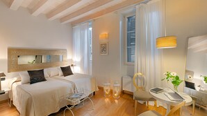A well-lit hotel room with two beds, a desk with a laptop, a chair, and a small table. - Gallery Room (Verona)