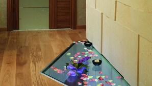 A hallway with a wooden door, a glass table with flowers and candles, and a textured wall. - Gallery Room (Verona)