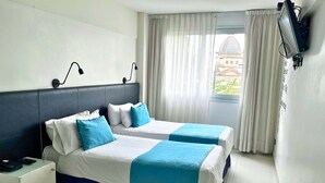Habitación de hotel con dos camas, un escritorio, un televisor y una ventana con cortinas.