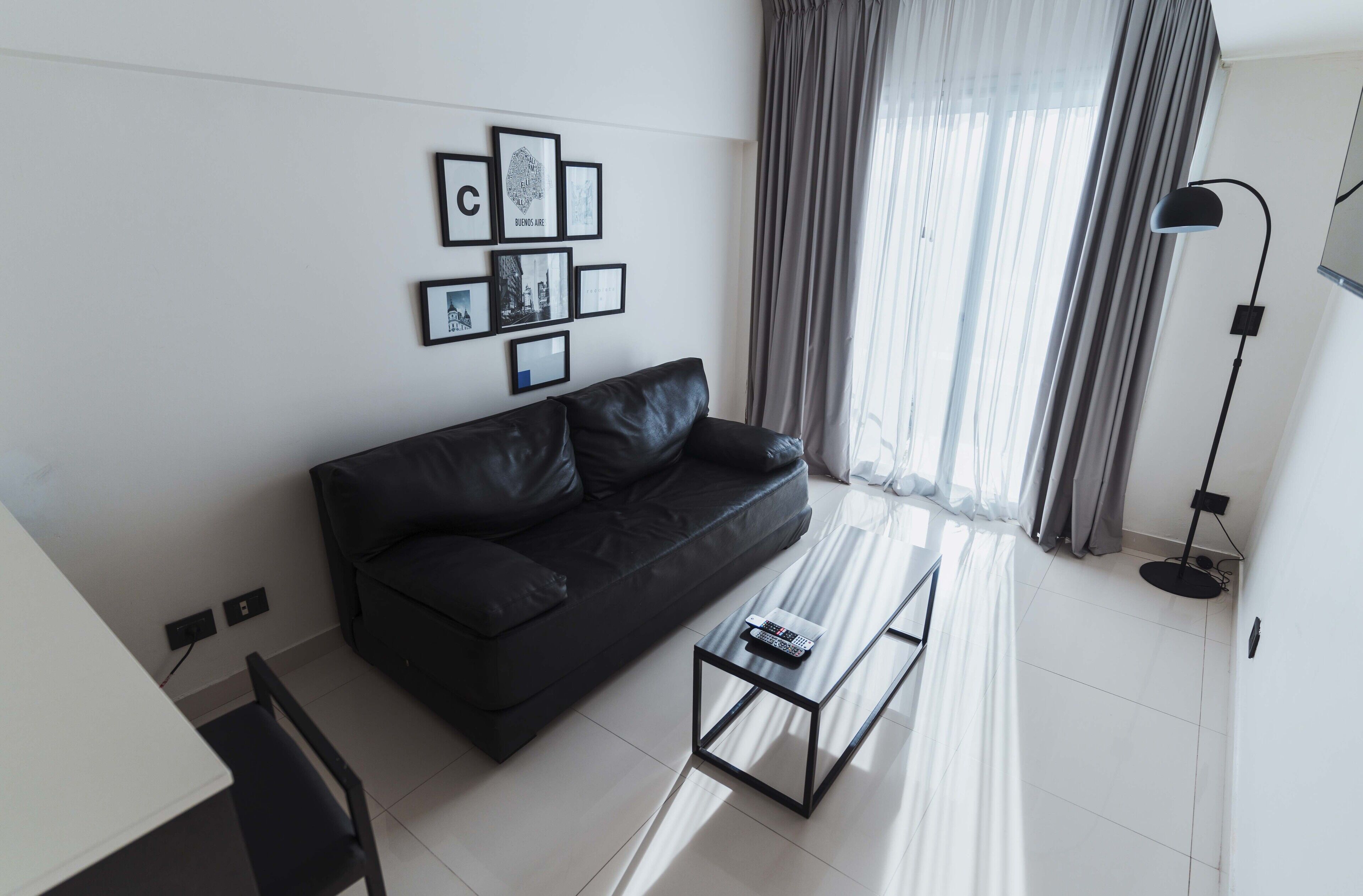 A modern living room with a black sofa, a glass coffee table, and a wall with framed pictures.