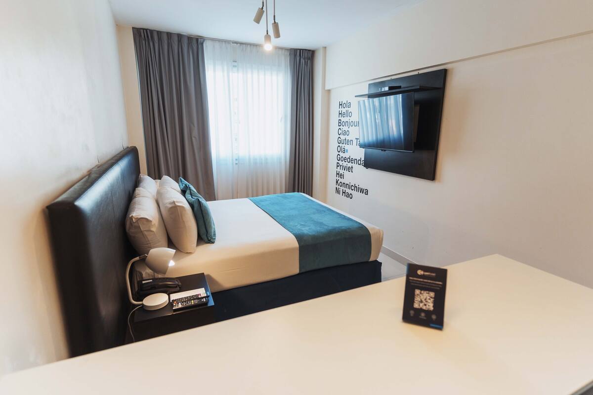 A modern hotel room with a bed, bedside table, and a mounted TV.