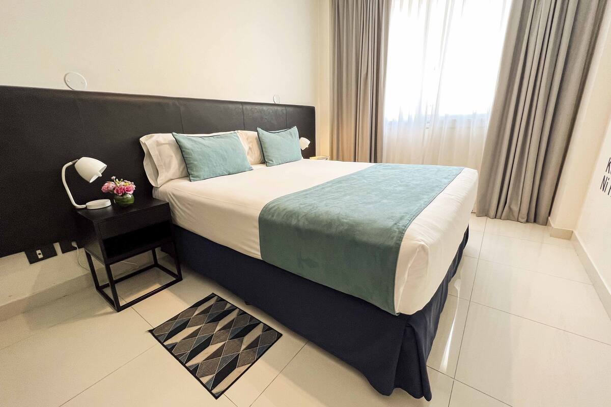 A hotel room with a bed, a nightstand, a lamp, and a vase with flowers.