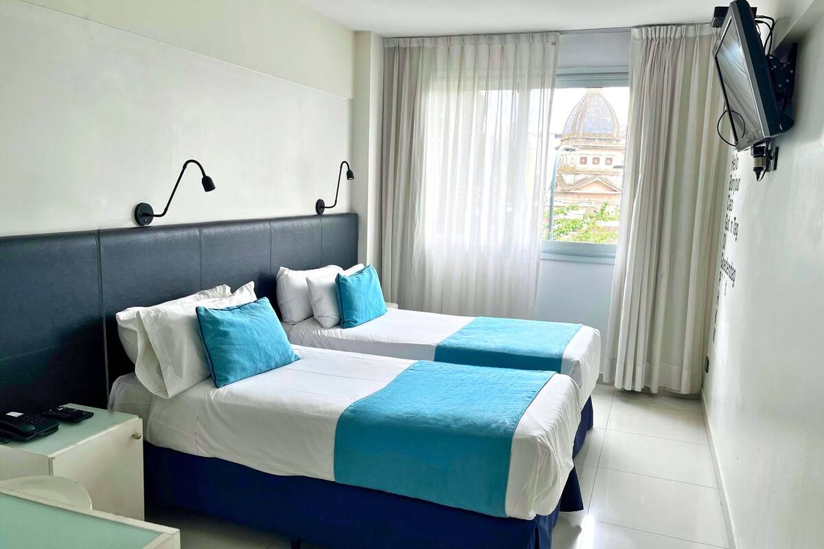 A hotel room with two beds, a desk, a TV, and a window with curtains.