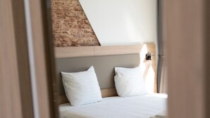 A bedroom with a bed, white bedding, a headboard, and a brick wall. - Plantage Hortus Apartments (Amsterdam)