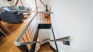A wooden staircase with metal railings, a wooden floor, and a living area with a sofa and cushions. - Plantage Hortus Apartments (Amsterdam)