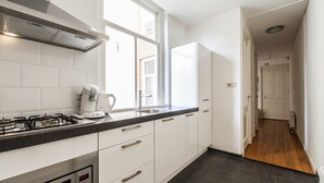 A modern kitchen with white cabinets, a gas stove, a microwave, and a coffee maker. - Plantage Hortus Apartments (Amsterdam)
