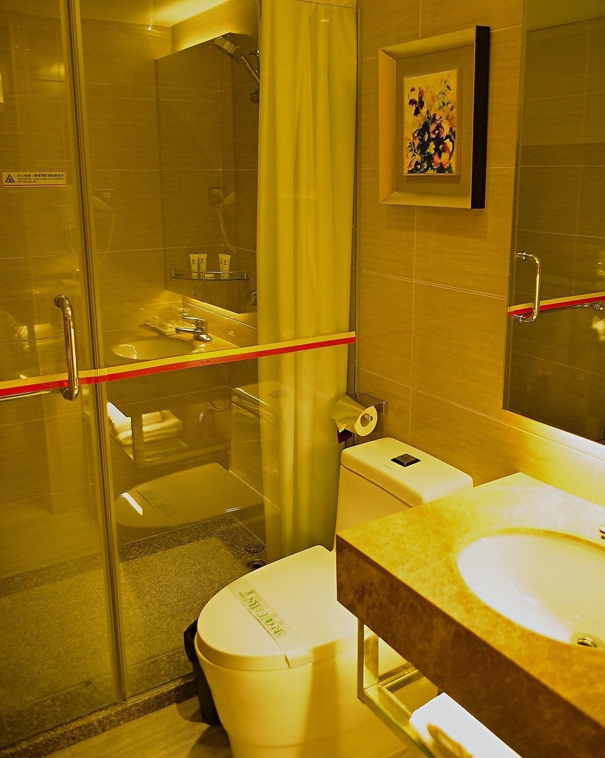 A hotel bathroom with a glass shower enclosure, a toilet, a sink, and a mirror.