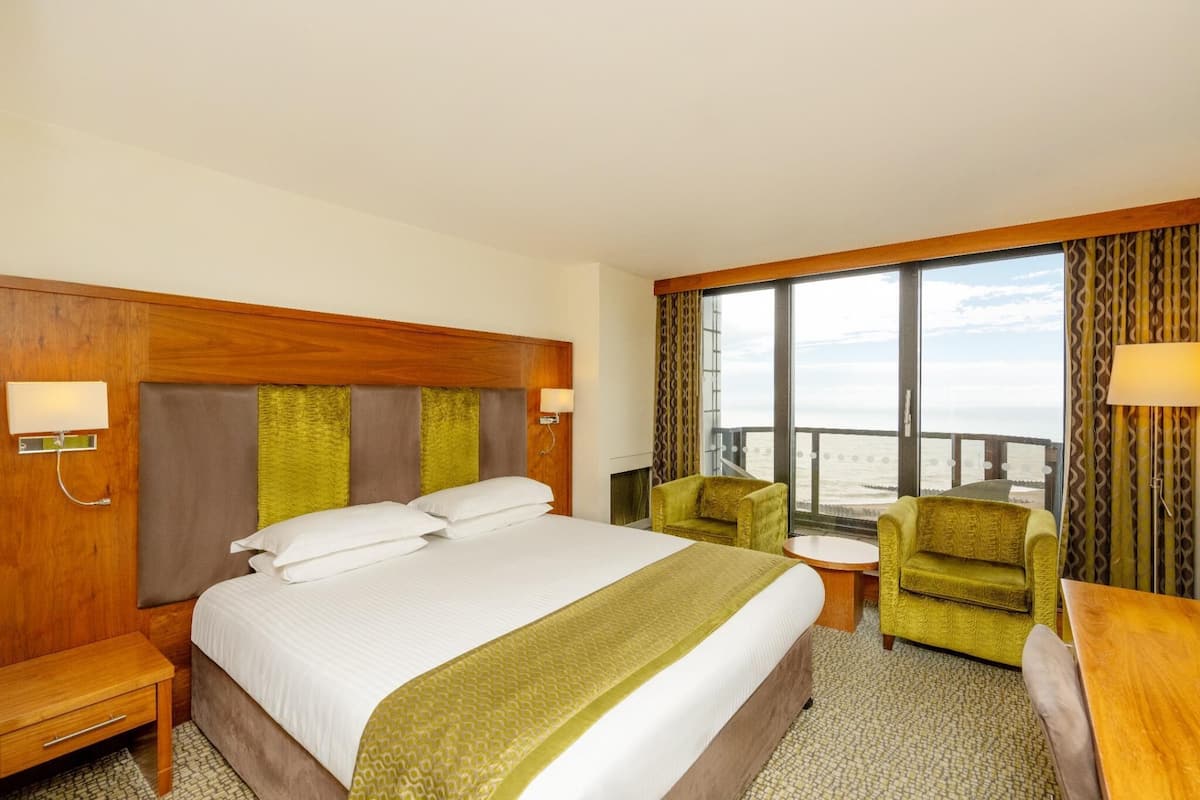 A hotel room with a large bed, a small table, two chairs, and a view of the ocean.