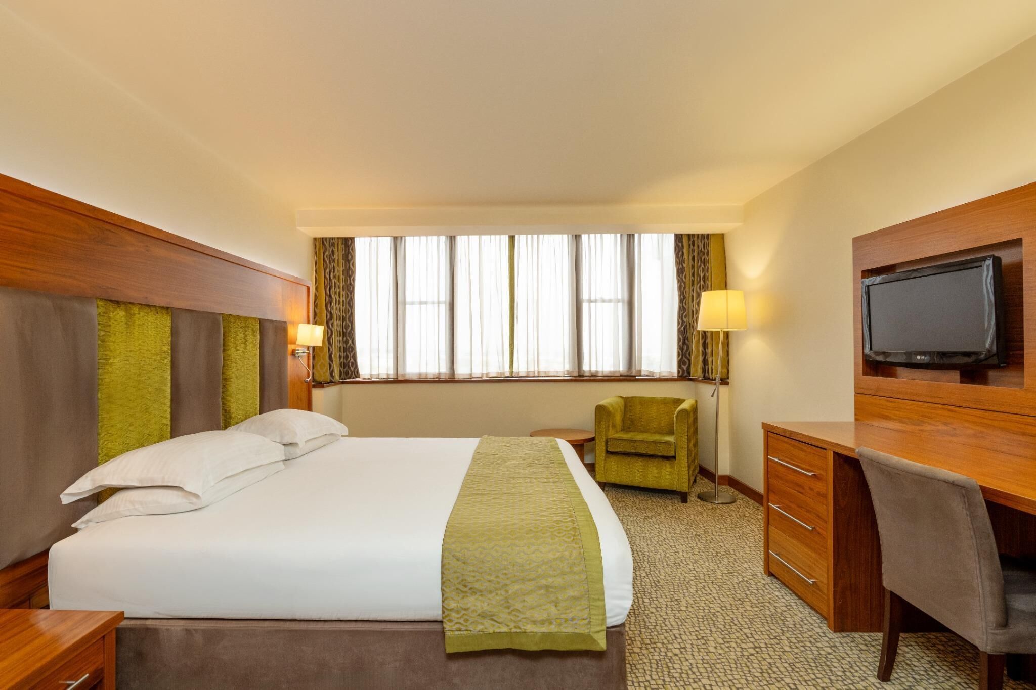 A hotel room with a bed, a desk, a chair, a television, and a window with curtains.