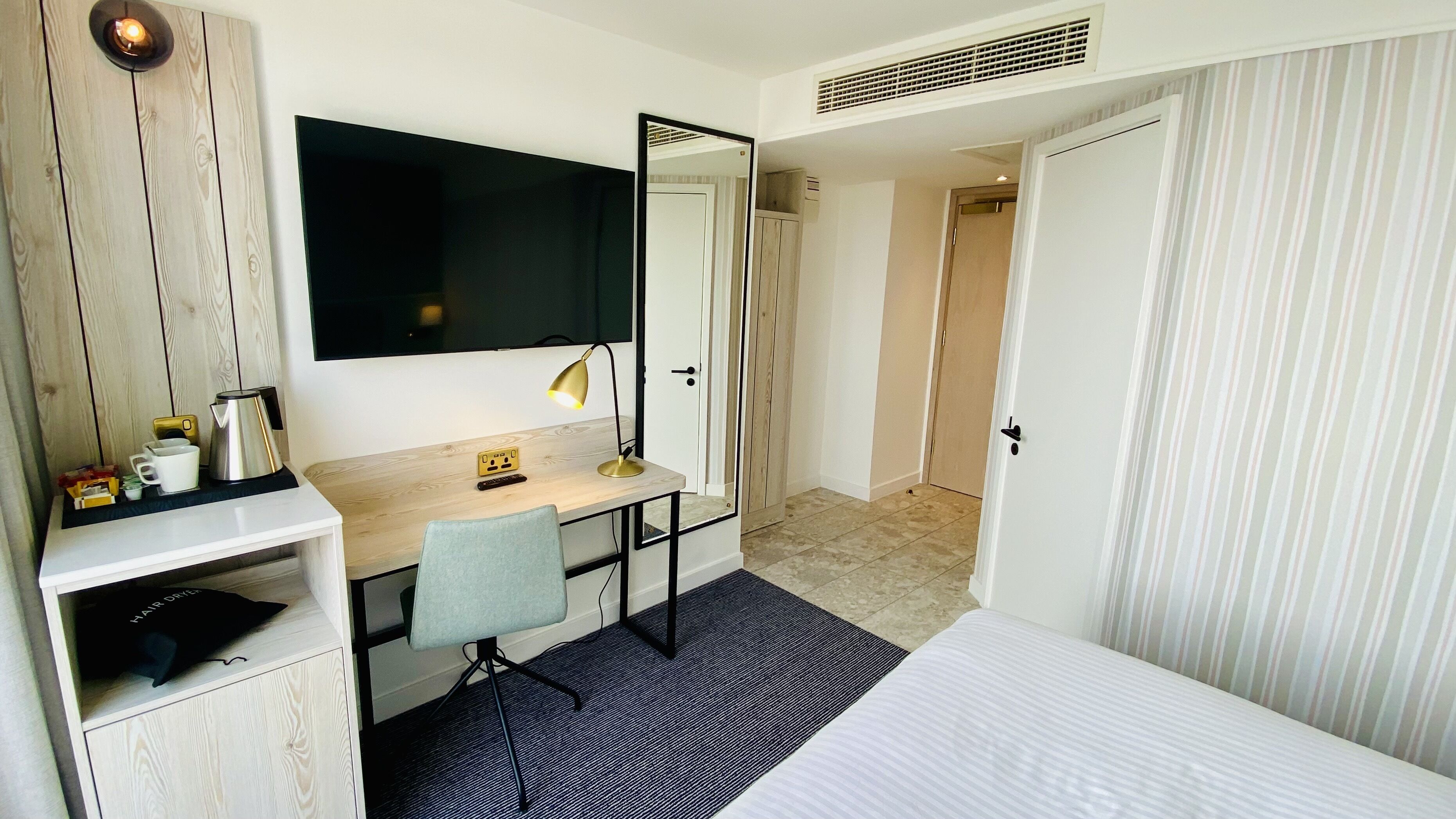 Habitación de hotel con cama, escritorio con silla, televisor, espejo, armario y puerta de baño.