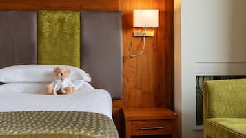 A hotel room with a bed, a bedside table, a lamp, a green chair, and a wall with a patterned design.