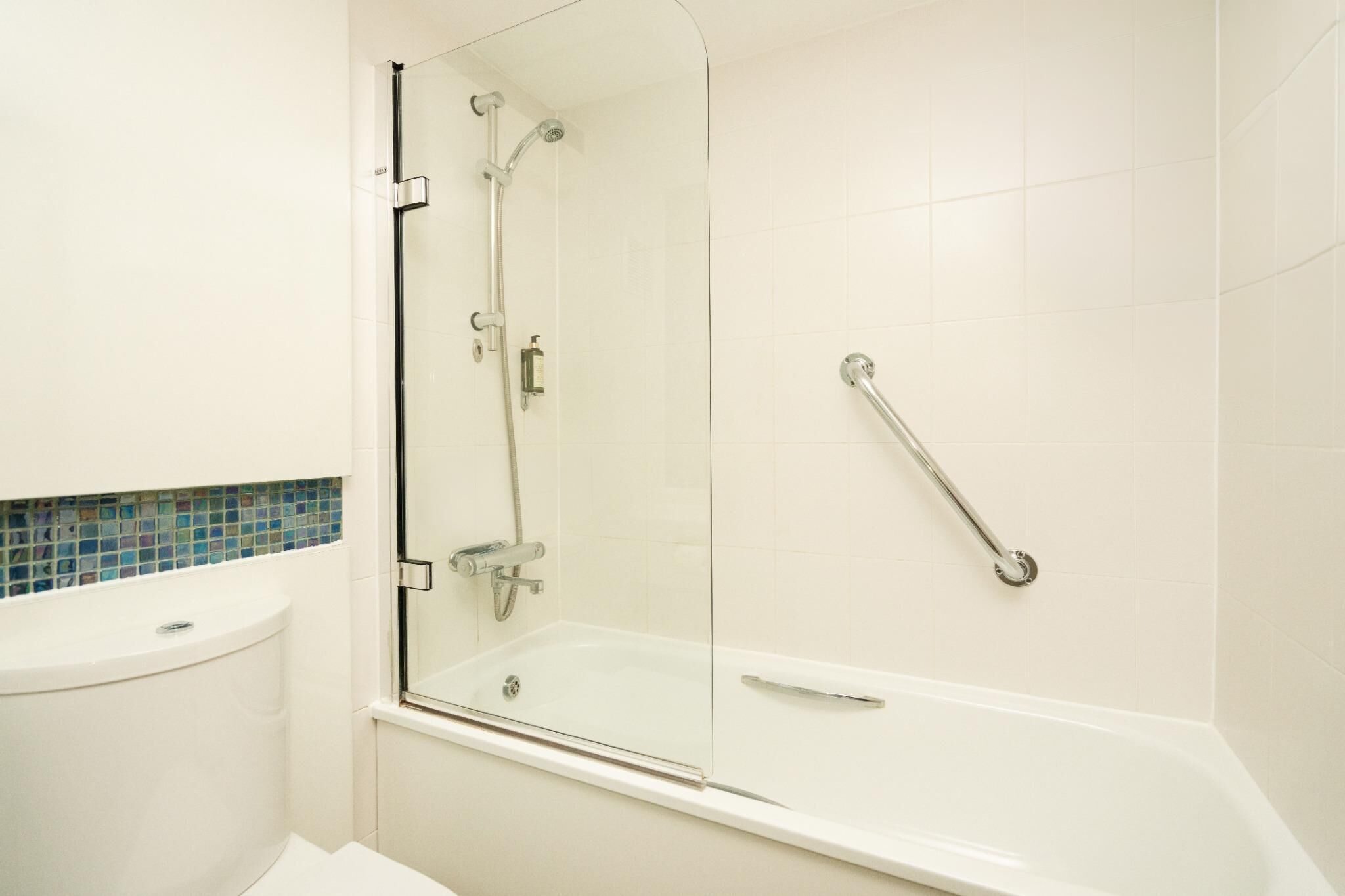 A bathroom with a glass shower enclosure, a white bathtub, and a handrail.