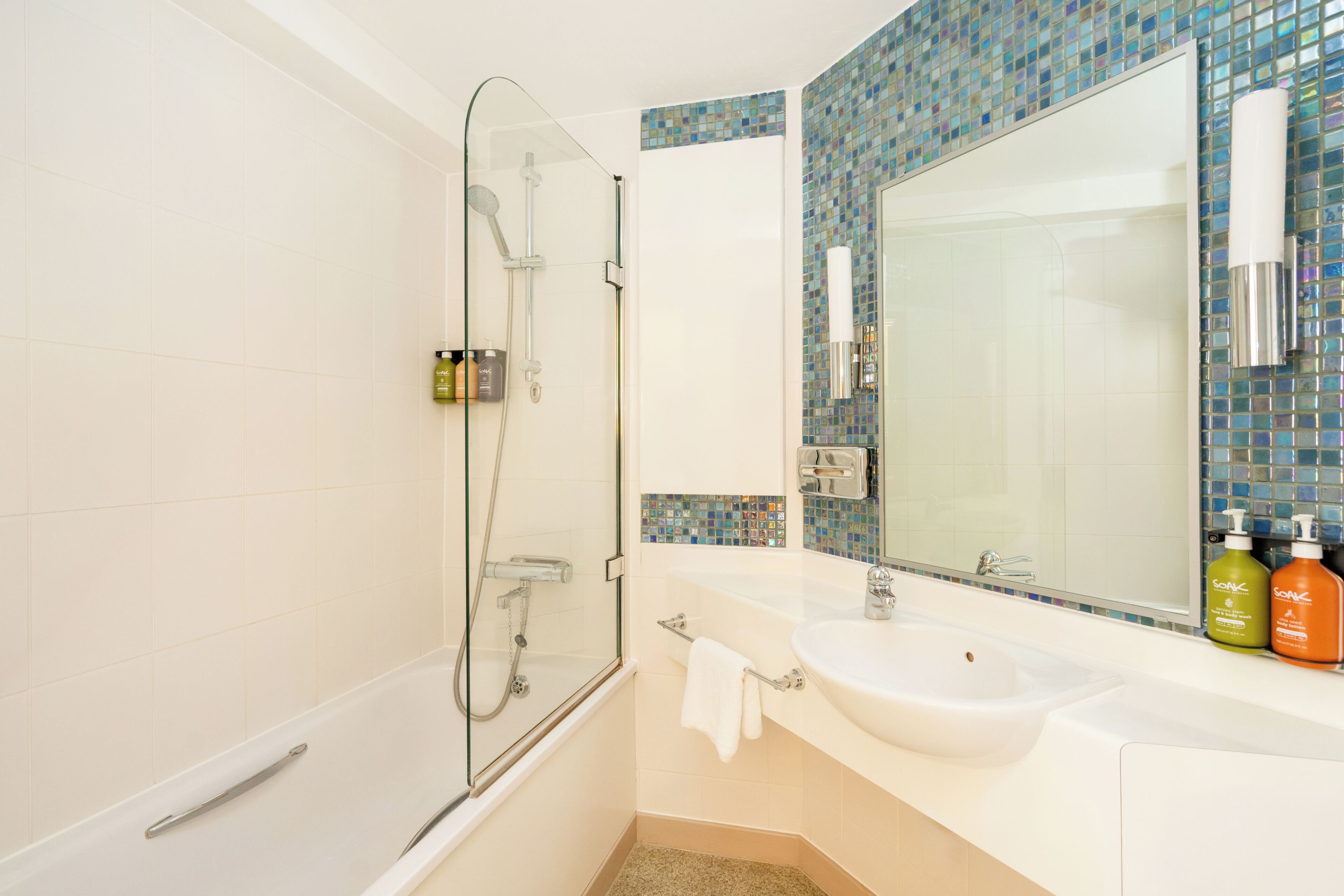A bathroom with a glass-enclosed shower, a white sink, and a mirror with a mosaic backsplash.