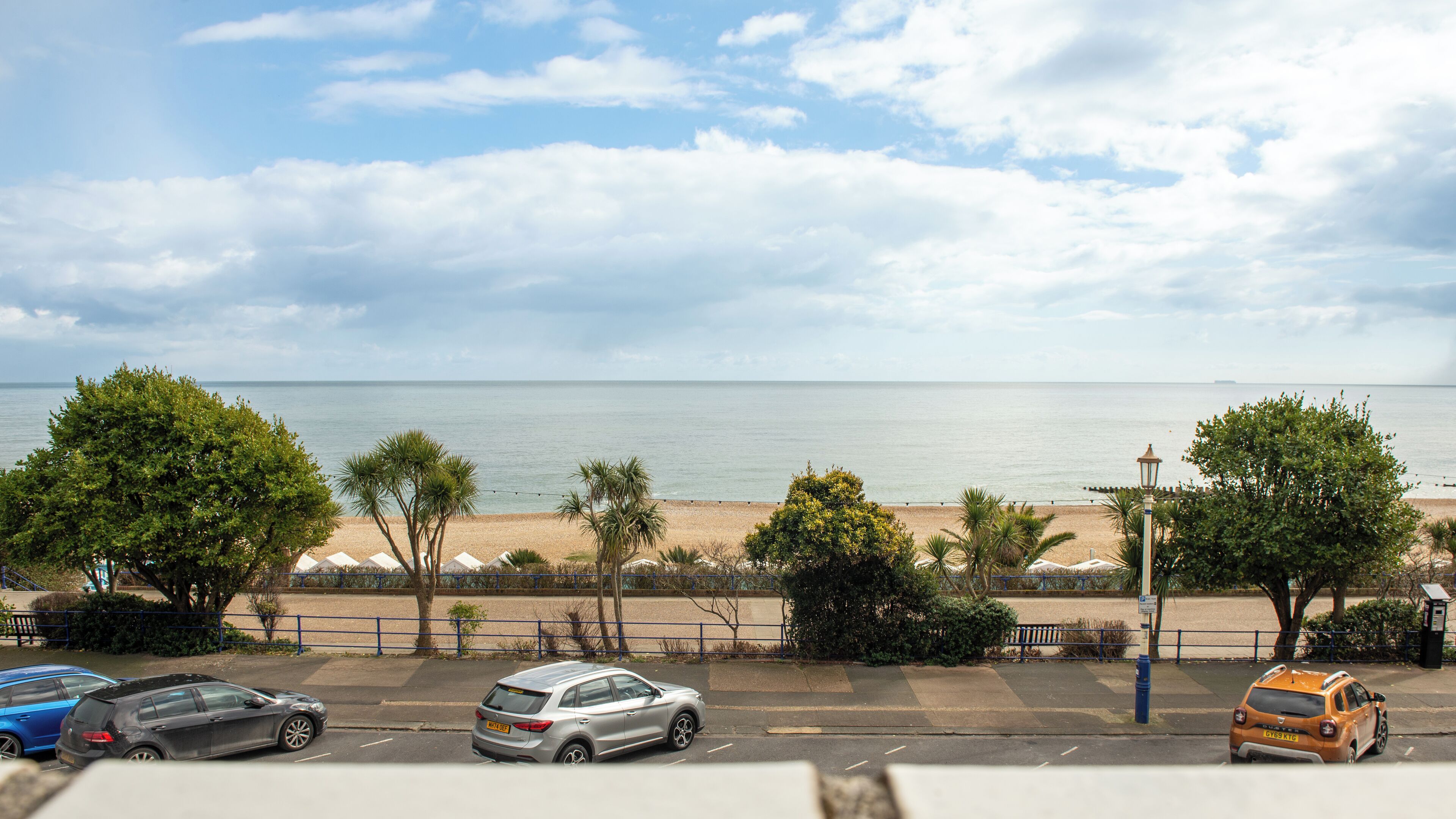 A beach view with a parking lot, cars, and a lamp post.