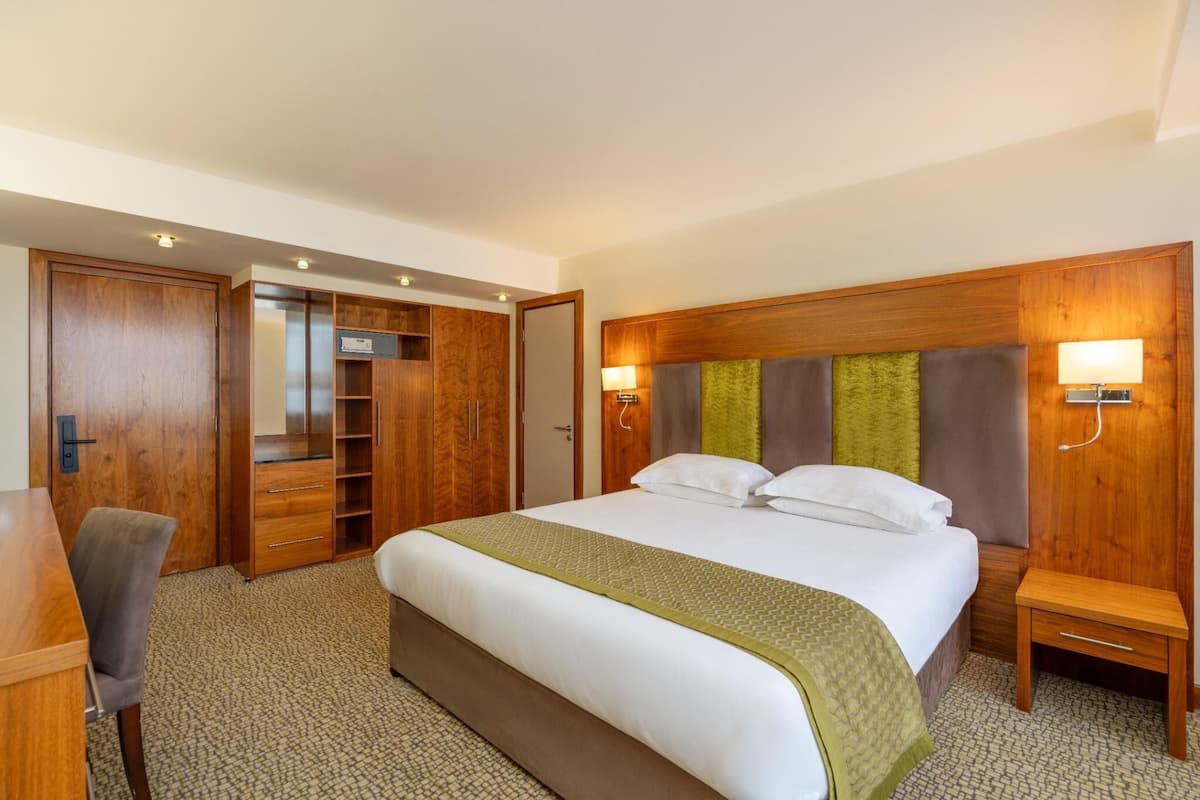A hotel room with a large bed, wooden wardrobe, a desk, and a chair.