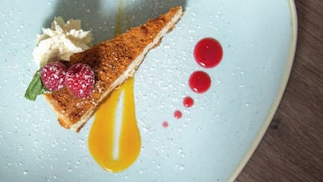 A dessert on a plate with a slice of cake, whipped cream, raspberries, and a drizzle of sauce.
