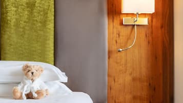 A neatly made bed with a teddy bear, a bedside lamp, and a wooden nightstand.
