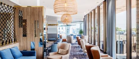 A modern hotel lobby with a blue sofa, beige armchairs, and a patterned carpet.