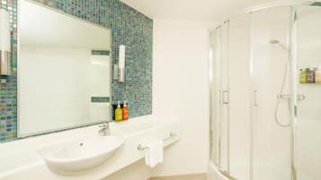Een badkamer met een wit wastafelmeubel, een grote spiegel, een douchecabine en een betegelde spatwand.