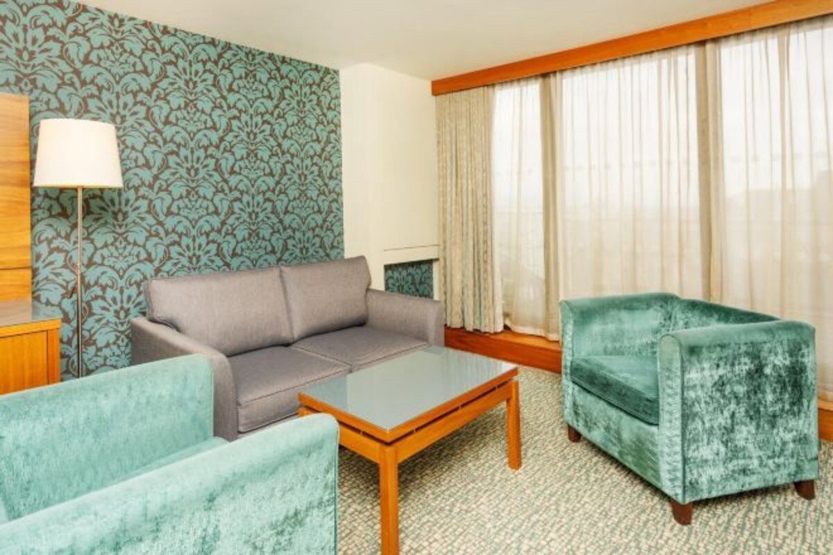 A hotel room with a sofa, armchair, and a small table.