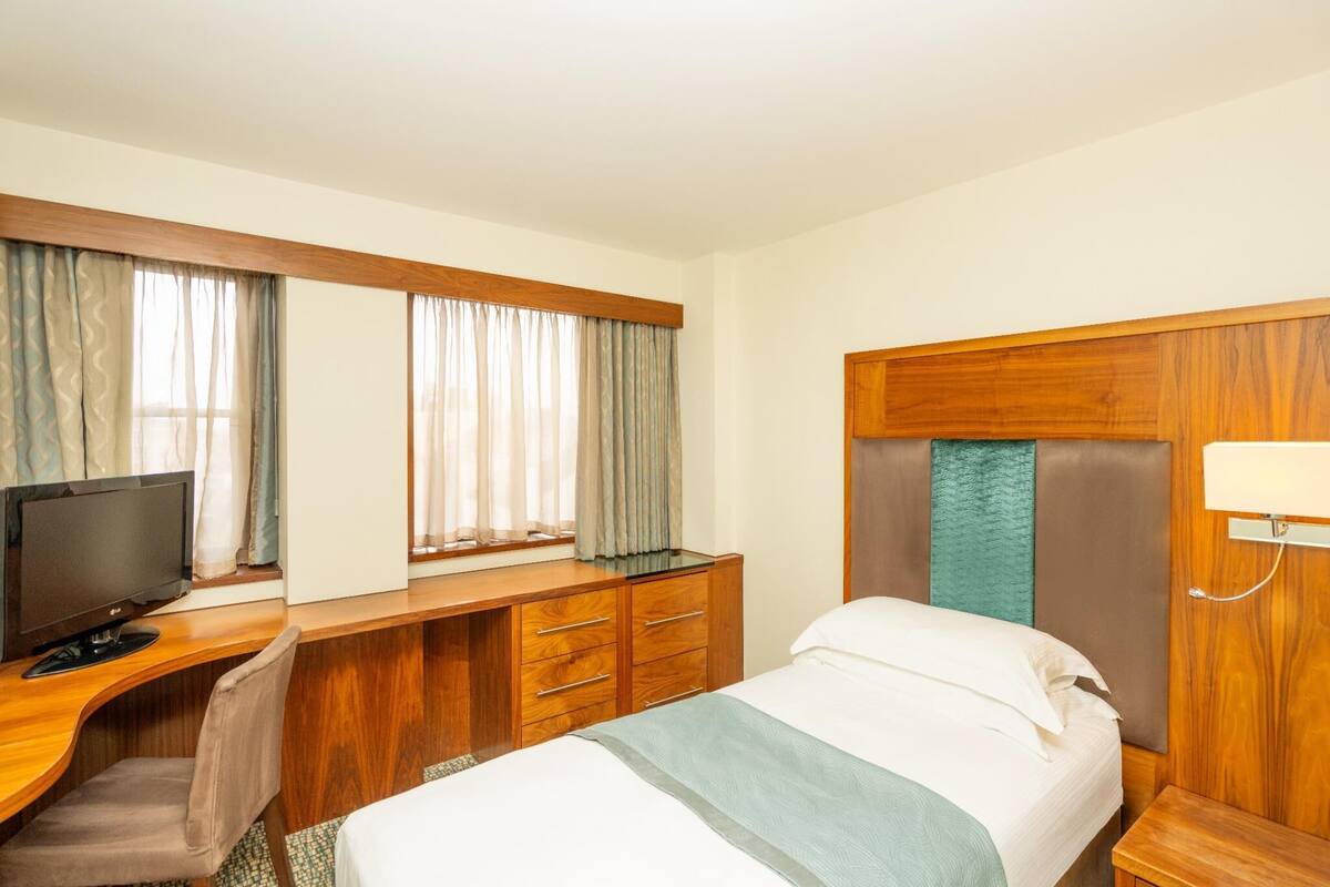 A hotel room with a bed, desk, television, and curtains.