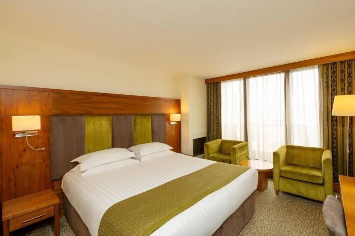 A hotel room with a large bed, two armchairs, a small table, and a nightstand.