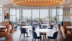 Een modern restaurant met ronde tafels en stoelen, grote ramen en een ronde lamp boven het plafond.