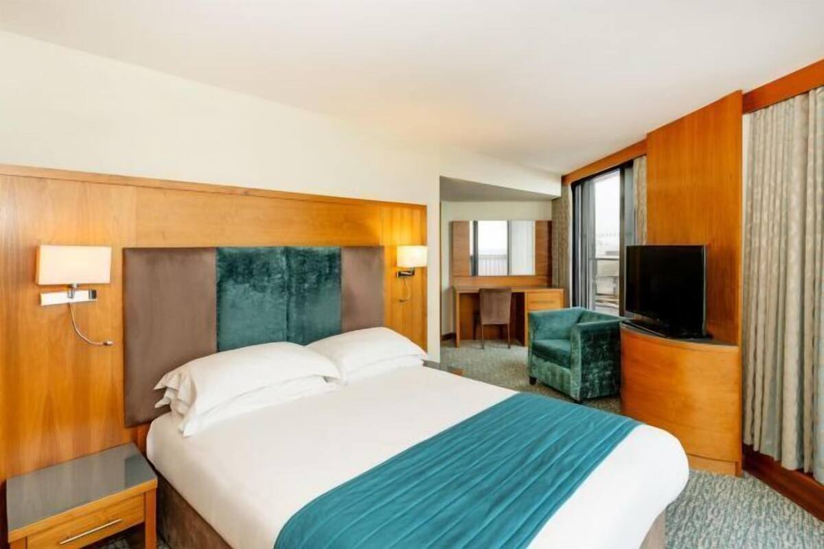 A hotel room with a bed, bedside tables, a desk with a chair, a television, and a window with curtains.