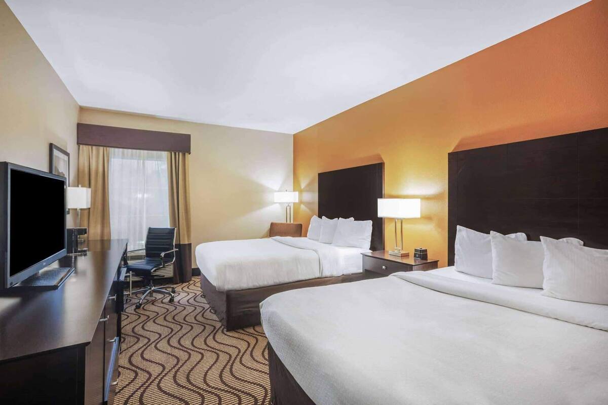A hotel room with two beds, a desk with a television, and a chair.