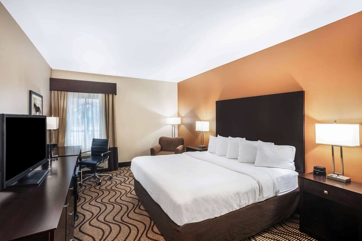 A hotel room with a large bed, a desk with a computer, a chair, and two lamps.