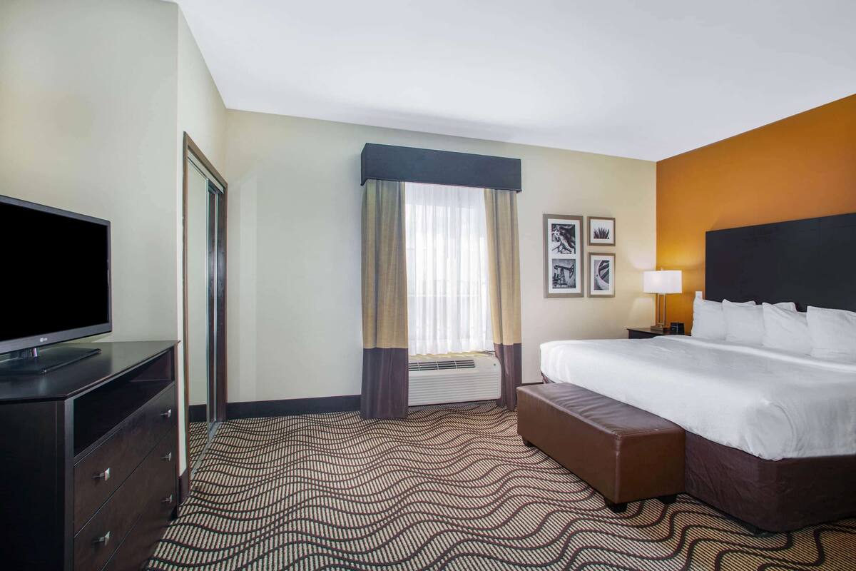 A hotel room with a bed, a TV, a desk, a chair, and a window with curtains.