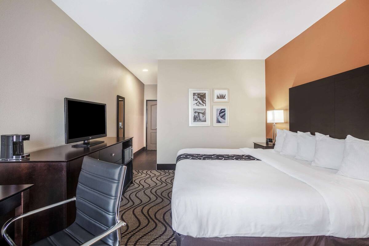 A hotel room with a bed, a desk with a TV, a chair, and a lamp.